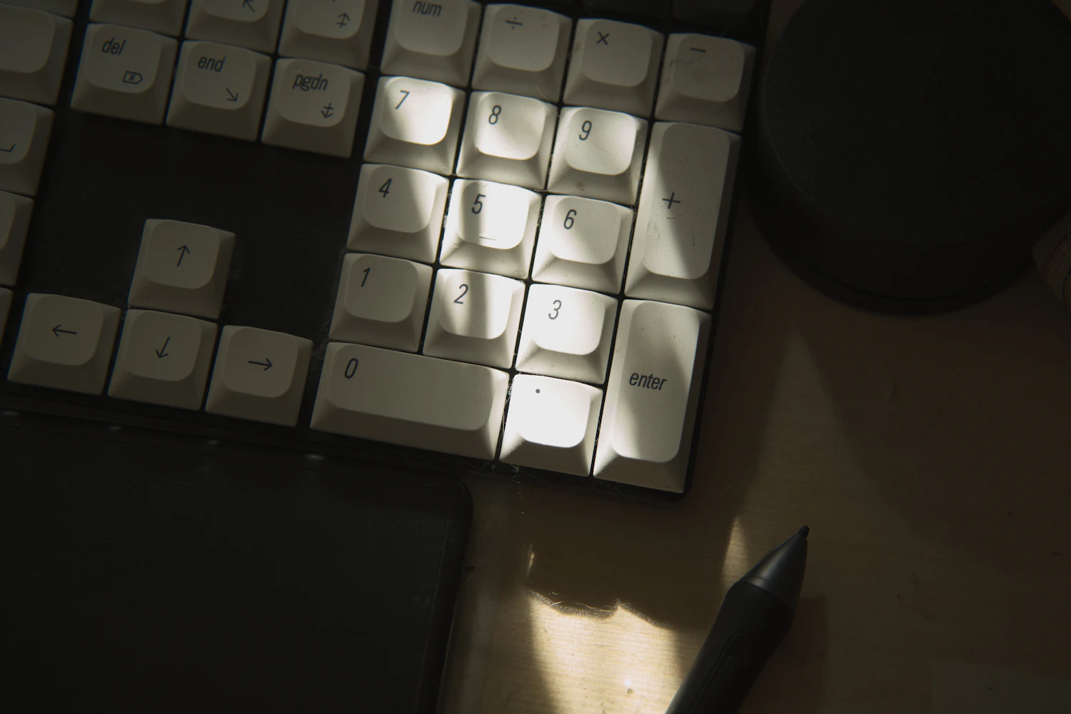 A white keyboard and pen crossed by a narrow beam of sunlight