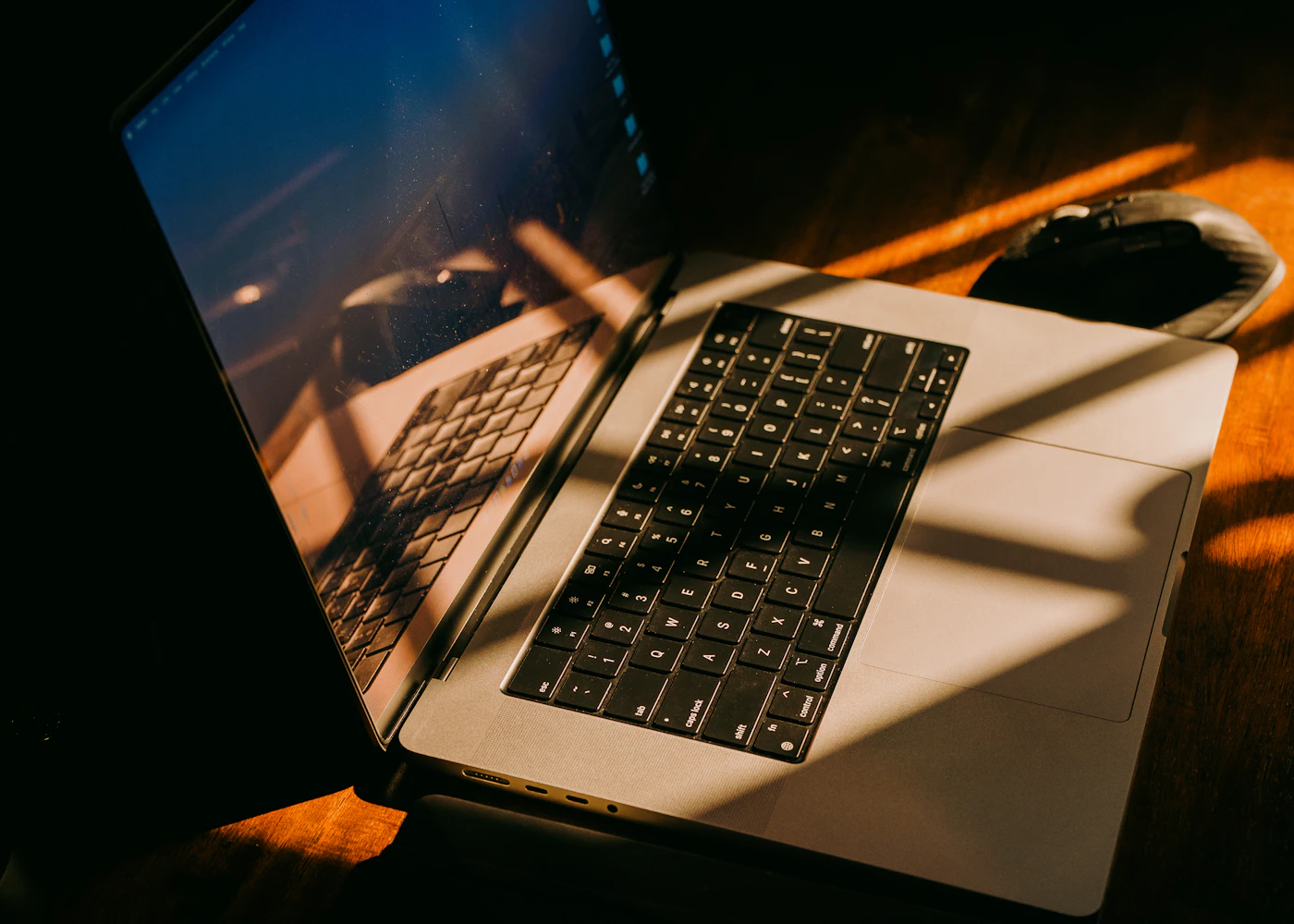 A laptop and keyboard crossed by warm window light